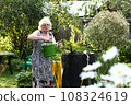 pensioner blond woman with water can on beautiful garden background closeup photo 108324619