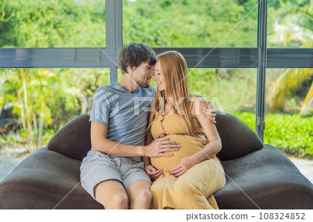 A tender moment captured as a husband and pregnant wife sit on the sofa, sharing an affectionate hug, their love and anticipation radiating in their embrace A tender moment captured as a husband and pregnant wife sit on the sofa, sharing an affectionate hug, their love and anticipation radiating in their embrace 108324852