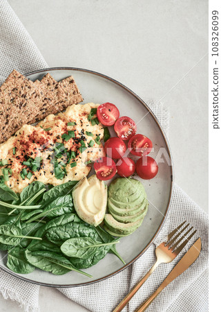 Scramble eggs with cherry tomatoes, fresh spinach leaves, avocado and crispbreads 108326099