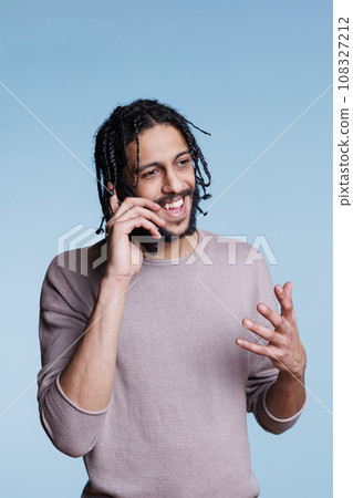 Cheerful arab man having fun conversation on smartphone and gestuculating with hand. Happy smiling person with carefree facial expression wearing casual clothes talking on mobile phone Cheerful arab man having fun conversation on smartphone and gestuculating with hand. Happy smiling person with carefree facial expression wearing casual clothes talking on mobile phone 108327212