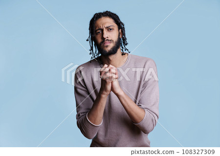 Arab man with clenched hands looking at camera with pleading facial expression. Person praying with folded arms gesture while asking for forgiveness with hopeful emotions 108327309