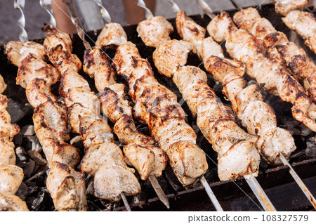 Traditional Turkish kebab cooked outdoors on skewers over hot grill with burning fire Traditional Turkish kebab cooked outdoors on skewers over hot grill with burning fire 108327579