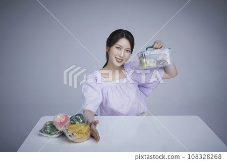 Image of a korean asain beautiful woman holding a plastic tub of fruits and vegetables wrapped in saran wrap. 108328268