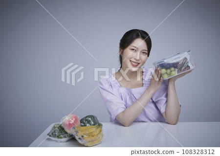 Image of a korean asain beautiful woman holding a plastic tub of fruits and vegetables wrapped in saran wrap. 108328312