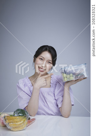 Image of a korean asain beautiful woman holding a plastic tub of fruits and vegetables wrapped in saran wrap. 108328321