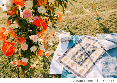 Boho style wedding arch stands over homespun blankets and pillows on a green lawn 108328857