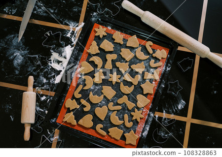 Raw Christmas cookies of different shapes lie on a tray on the table Raw Christmas cookies of different shapes lie on a tray on the table 108328863