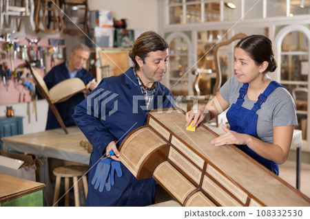 Employee supports lid of chest of drawers while helping his female colleague restore furniture Employee supports lid of chest of drawers while helping his female colleague restore furniture 108332530