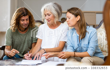 Happy couple and mature lady writing down plans on the sofa at cosy home Happy couple and mature lady writing down plans on the sofa at cosy home 108332653