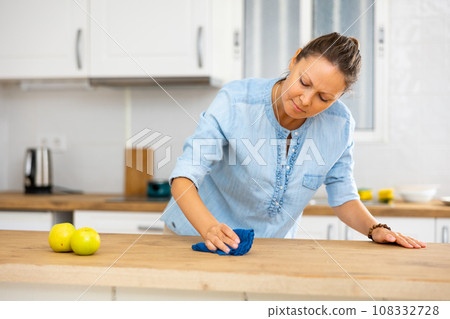 Focused woman cleaning kitchen table at home Focused woman cleaning kitchen table at home 108332728