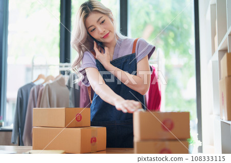 Starting small business entrepreneur of independent Asian female online seller talking on the phone with a customer and packing products for delivery to the customer. and SME delivery concept. Starting small business entrepreneur of independent Asian female online seller talking on the phone with a customer and packing products for delivery to the customer. and SME delivery concept. 108333115