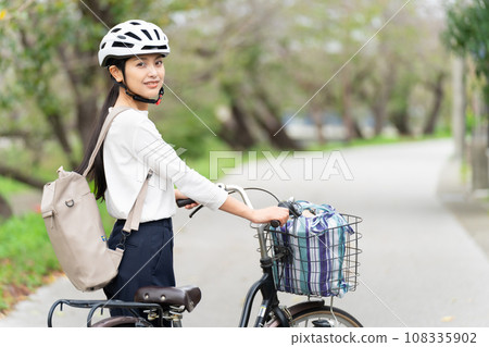 A young woman wearing a cycling helmet and walking with a bicycle 108335902