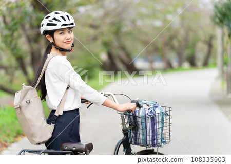 A young woman wearing a cycling helmet and walking with a bicycle 108335903