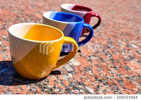 Time of ceremony for tea and coffee.Colorful cups on red marble surface Time of ceremony for tea and coffee.Colorful cups on red marble surface 108335984