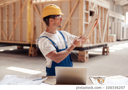 Handsome male builder in safety helmet holding wooden board 108336207