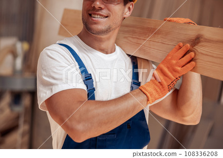 Joyful worker carrying timber wood plank at construction site Joyful worker carrying timber wood plank at construction site 108336208
