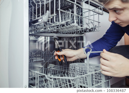 Dishwasher repair. A service center representative diagnoses and repairs a dishwashing machine at home. Specialist in working with home appliances. Call a technician to your home. Close-up 108336487