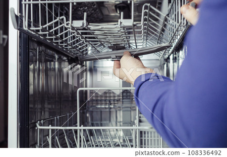 Dishwasher repair. A service center representative diagnoses and repairs a dishwashing machine at home. Specialist in working with home appliances. Call a technician to your home. Close-up 108336492