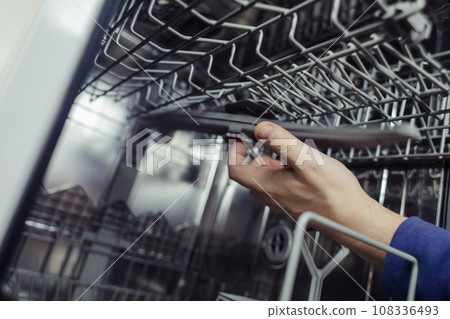 Dishwasher repair. A service center representative diagnoses and repairs a dishwashing machine at home. Specialist in working with home appliances. Call a technician to your home. Close-up Dishwasher repair. A service center representative diagnoses and repairs a dishwashing machine at home. Specialist in working with home appliances. Call a technician to your home. Close-up 108336493