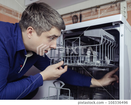 Dishwasher repair. A service center representative diagnoses and repairs a dishwashing machine at home. Specialist in working with home appliances. Call a technician to your home. Close-up Dishwasher repair. A service center representative diagnoses and repairs a dishwashing machine at home. Specialist in working with home appliances. Call a technician to your home. Close-up 108336496
