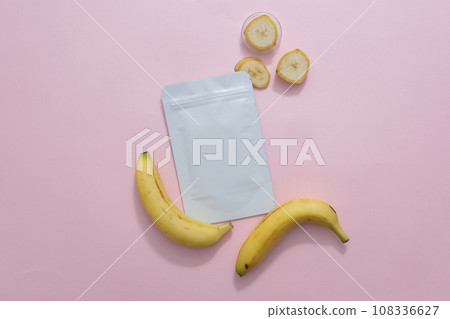 Top view of a facial sheet mask package decorated with banana and banana slices on a pink background. Minimalist concept for advertising cosmetic with natural ingredient  108336627