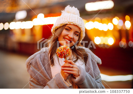 Young woman with caramel apple on Christmas market. Smiling woman in winter style clothes posing. 108337750