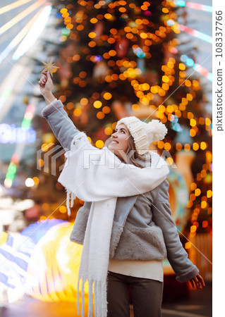Smiling woman in winter style clothes posing at festive street market. Woman enjoying winter moments 108337766