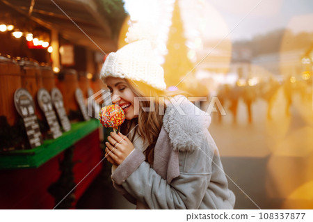 Young woman with caramel apple on Christmas market. Smiling woman in winter style clothes posing. Young woman with caramel apple on Christmas market. Smiling woman in winter style clothes posing. 108337877