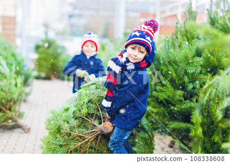 Two little sibling kid boys holding christmas tree. Happy children in winter clothes choosing and buying xmas tree in outdoor shop. Family, tradition, celebration concept. Two little sibling kid boys holding christmas tree. Happy children in winter clothes choosing and buying xmas tree in outdoor shop. Family, tradition, celebration concept. 108338608