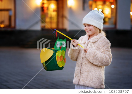 Little preschool kid girl holding selfmade traditional owl lanterns with candle for St. Martin procession. child happy about children and family parade in kindergarten. German tradition Martinsumzug 108338707