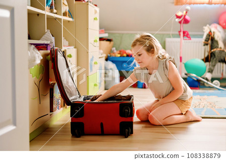 Little girl packing suitcase at home. Cute child putting clothes into suitcase. Preparing for family vacations with children. Practicing independence 108338879