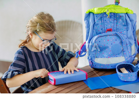 Happy smiling girl preparing for school her backpack. First day of school. Back to school concept. Little child collecting different supplies like pens and books in a bag or satchel. 108338880