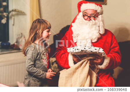 Little toddler girl talking to Santa Claus called Nikolaus or Weihnachtsmann in German. Happy smiling kid waiting for gifts. Santa with golden book. Xmas, childhood, holiday 108339048