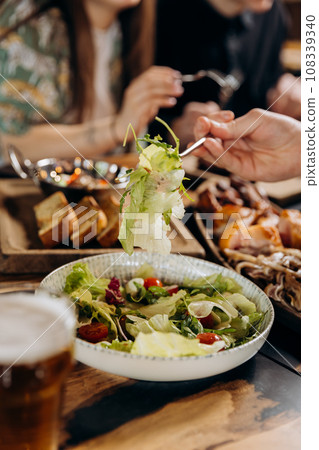 Close up of male hands eating fresh tasty salad in restaurant during dinner with friends 108339340