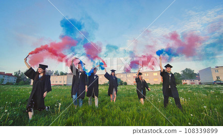 Graduates in costume walk with a smoky multi-colored smoke at sunset Graduates in costume walk with a smoky multi-colored smoke at sunset 108339899