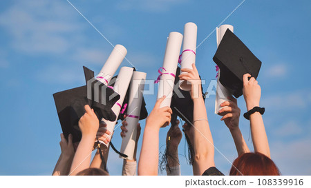 College graduates raise their hands with caps and diplomas to the sky. 108339916