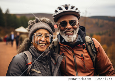 An elderly African American couple rides bicycles, enjoying the mountain landscape, man and woman wearing a helmet, healthy lifestyle concept. An elderly African American couple rides bicycles, enjoying the mountain landscape, man and woman wearing a helmet, healthy lifestyle concept. 108341733