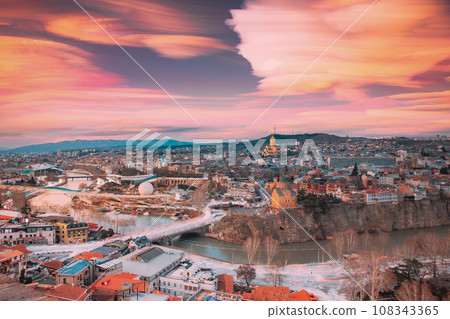 Tbilisi, Georgia. Amazing Cloud Trails In Sky. 6k Georgian Capital Skyline Cityscape. City During Sunset And Night Illuminations. Unusual Cloudy Effects Sky. Elevated Top View Of Famous Landmarks 108343365