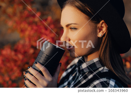 Hipster woman enjoys aroma fresh coffee. Drinking from thermos in autumn forest 108343960