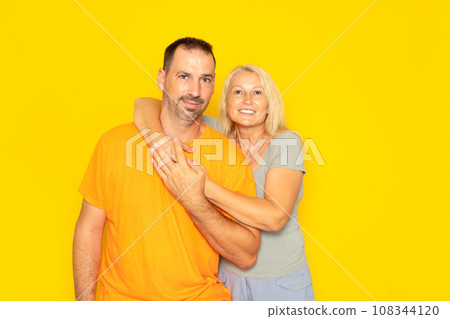 White happy couple hugging and looking at camera isolated over yellow background. 108344120