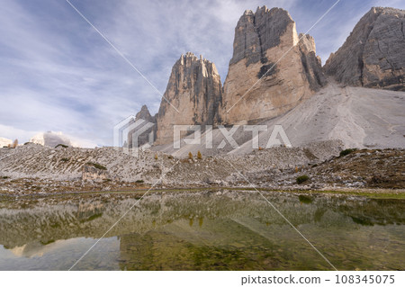 Massive rock formation of Tre Cime reflecting in small pond during autumn day, Dolomites, Italy Massive rock formation of Tre Cime reflecting in small pond during autumn day, Dolomites, Italy 108345075