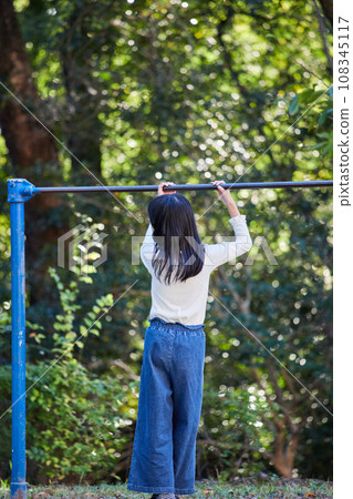 A state of an elementary school girl playing a horizontal bar in an autumn park A state of an elementary school girl playing a horizontal bar in an autumn park 108345117