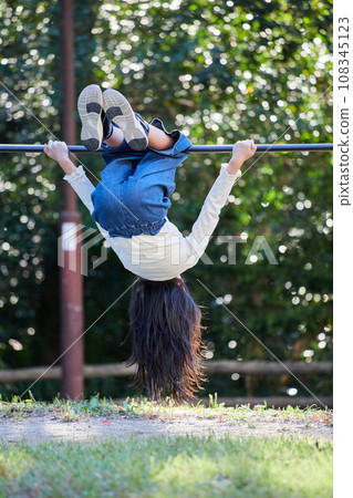 A state of an elementary school girl playing a horizontal bar in an autumn park A state of an elementary school girl playing a horizontal bar in an autumn park 108345123