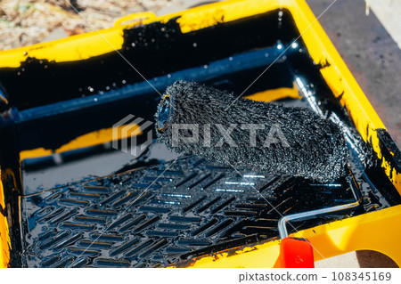 Paint roller in tray with black industrial paint or primer. Top view of paint roller with paint tray Paint roller in tray with black industrial paint or primer. Top view of paint roller with paint tray 108345169