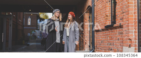 Banner Two girls walking on street together and holding their hands copy space. They are wearing spring or autumn clothes and they are happy. Friendship and relationship concept 108345364