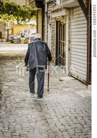 Elderly stooped man with stick walks along the street of old city. Back view 108345955