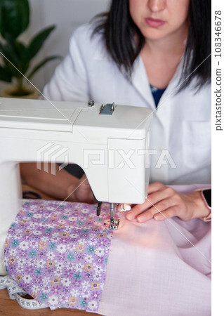 Young adult seamstress working on sewing machine. 108346678