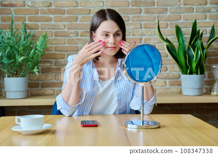 Young happy brunette looking at her face in mirror Young happy brunette looking at her face in mirror 108347338