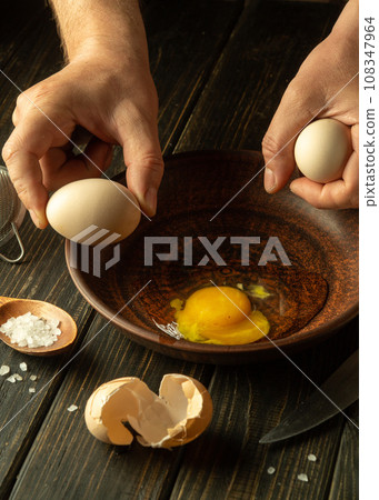 Delicious omelet by the chef hands in the restaurant kitchen. The cook tries to crack an egg on the plate before cooking. Egg breakfast. Delicious omelet by the chef hands in the restaurant kitchen. The cook tries to crack an egg on the plate before cooking. Egg breakfast. 108347964