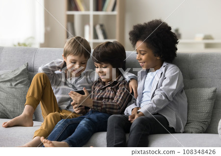 Diverse kids sit on sofa use smartphone Diverse kids sit on sofa use smartphone 108348426